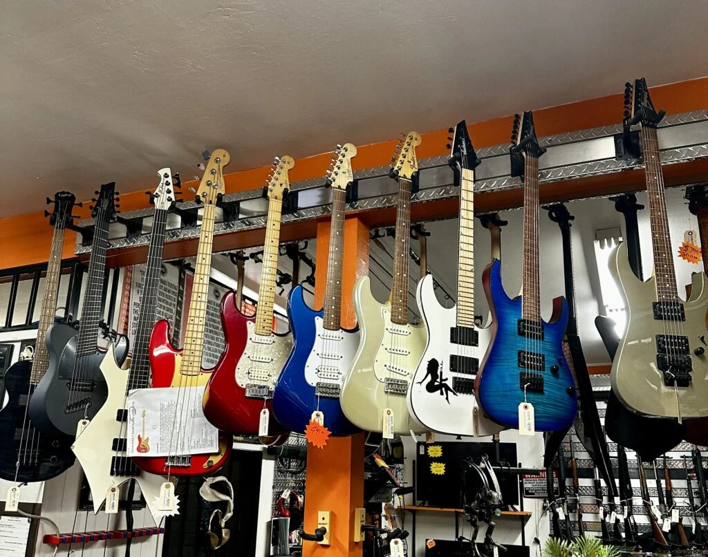 A rack of electric and bass guitars hanging on the shop's orange wall
